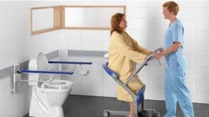 paciente que va al cuarto de baño sentado en una plataforma de traslado con ruedas que maneja una cuidadora