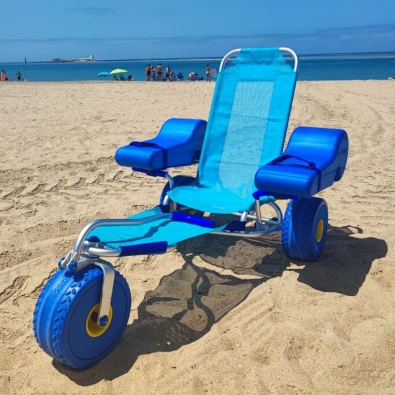 Silla de ruedas anfibia azul con ruedas balón sobre la arena, en playa accesible lista para baño asistido