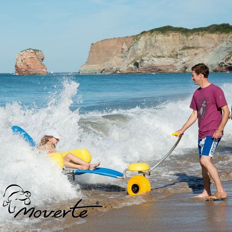 Baño asistido con silla de ruedas anfibia Tiralo 2, con ruedas balón y flotadores, entrando al mar en una playa accesible